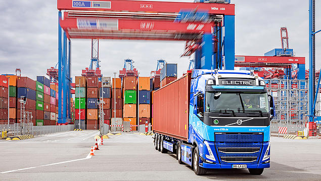 Ein E-Lkw des Container-Transport-Dienstes (CTD) am HHLA Container Terminal Burchardkai in Hamburg, im Hintergrund Containerbrücken und Containerstapel.