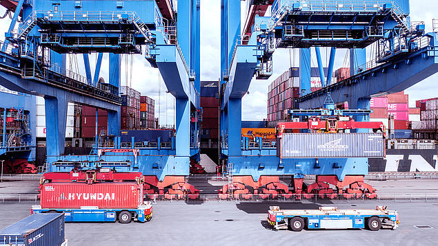 Zwei fahrerlose Transportfahrzeuge (AGV) bewegen Container unter einer Containerbrücke am HHLA Container Terminal Altenwerder in Hamburg.